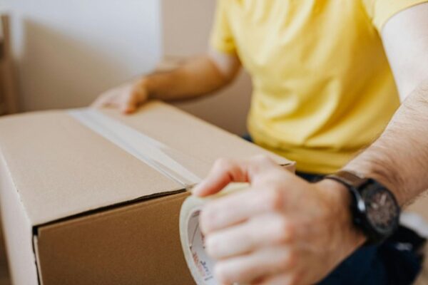 Person sealing a cardboard box with packing tape, preparing a package for shipping or moving.