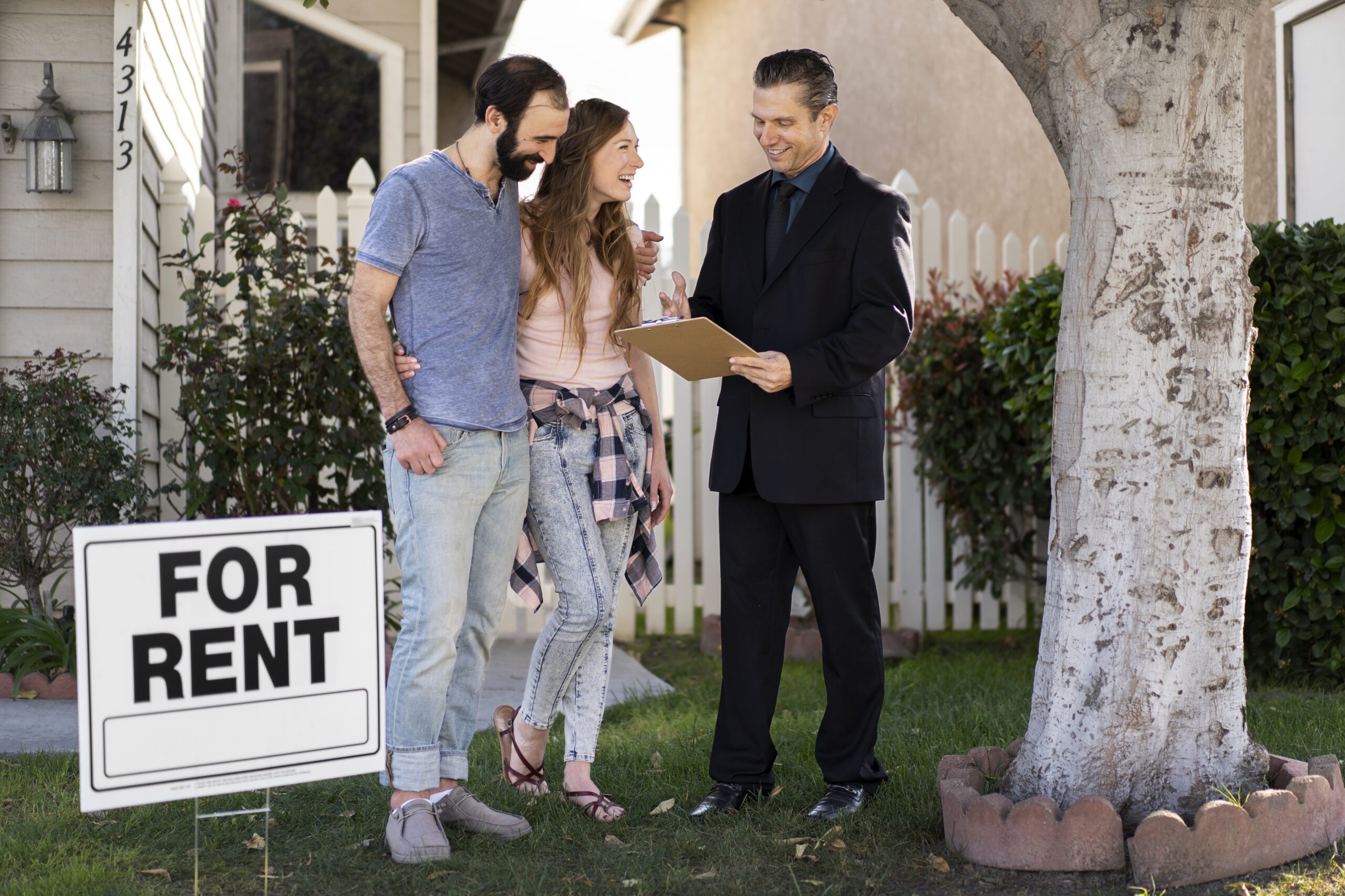 Real estate agent discussing rental agreement with a couple outside a house with a 'For Rent' sign