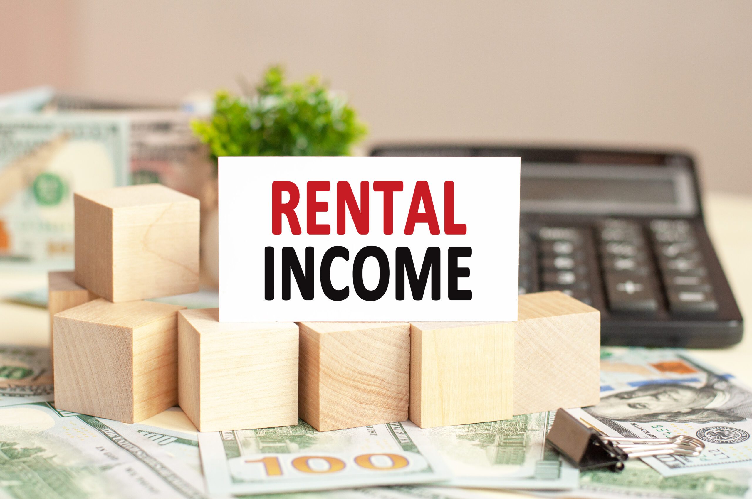 Paper card with text RENTAL INCOME. Calculator, flowers and brown background